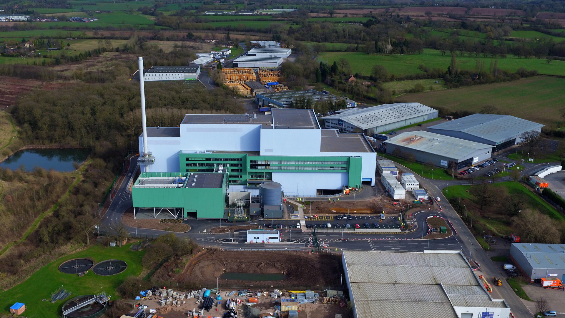 Luftaufnahme eines modernen Industriegebäudes mit grüner Fassade und angrenzenden Lagerhallen in Worcestershire, England.
