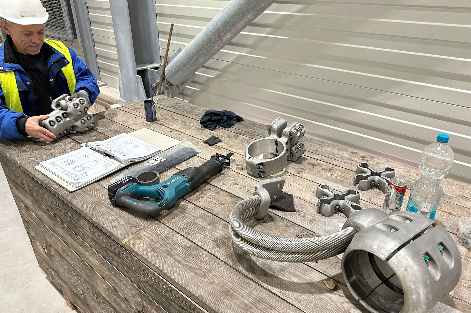Ein Arbeiter mit Sicherheitskleidung, der an einem Tisch mit verschiedenen Montagewerkzeugen und -teilen für Energiekabel arbeitet.