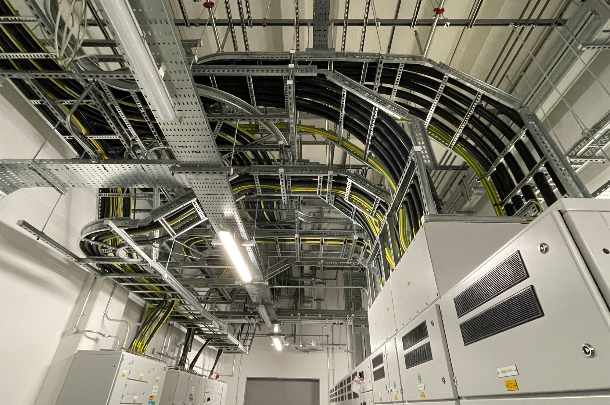 Komplexe Anordnung von Kabeltrassen und elektrischen Schaltschränken in einem technischen Raum.