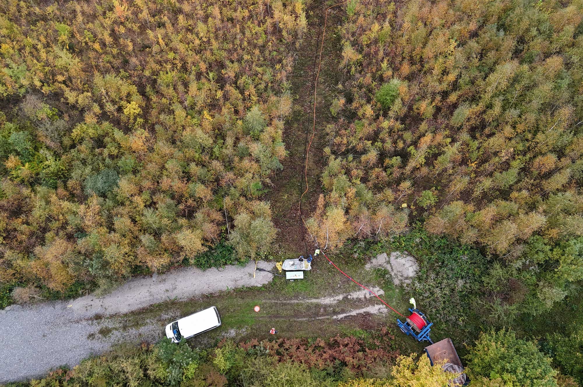Luftaufnahme einer Baustelle mit einem Fahrzeug und Ausrüstung zur Kabelmontage in einem bewaldeten Gebiet.
