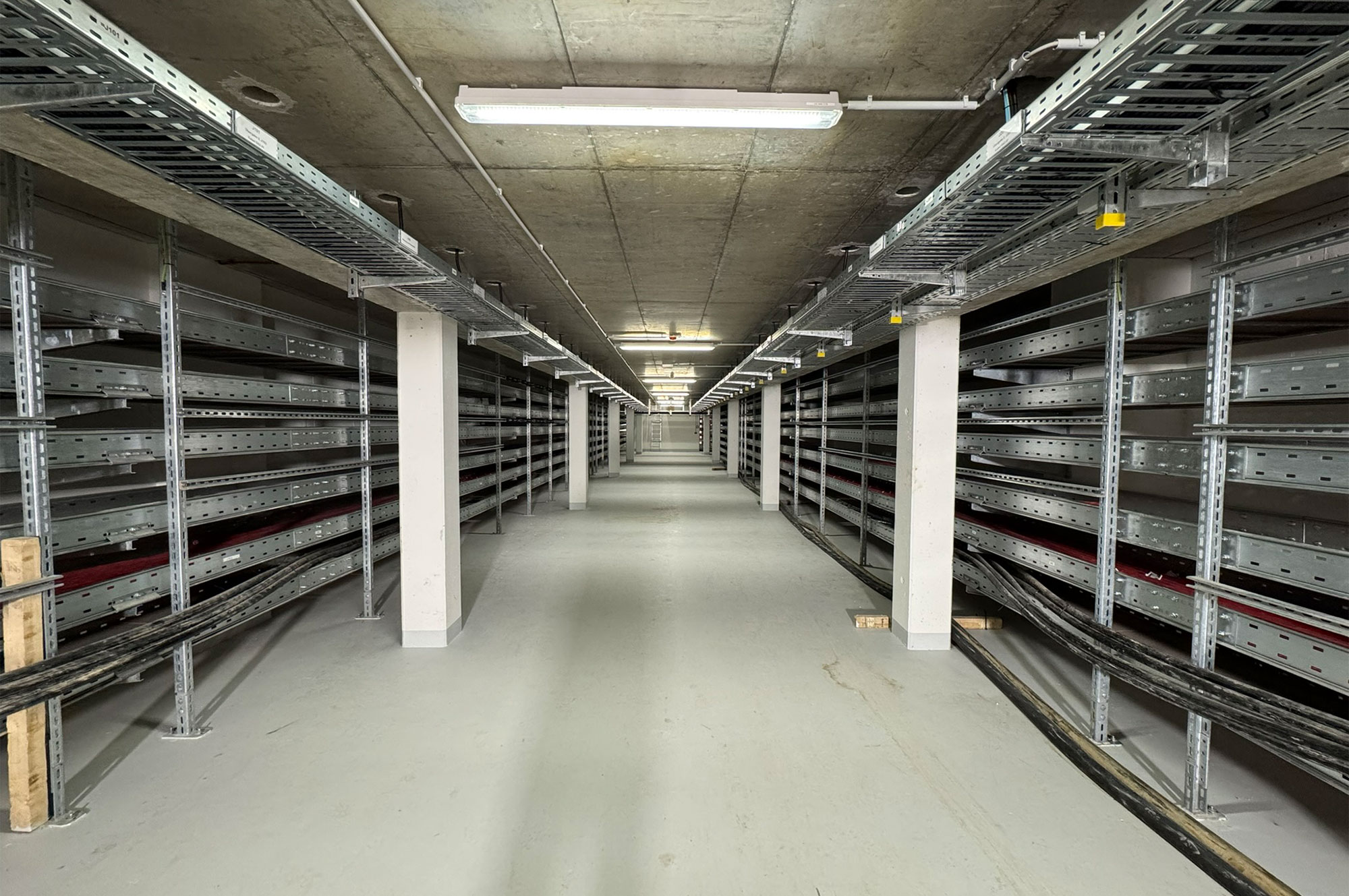 Blick auf einen langen, leeren Gang mit Metallregalen und einem grauen Boden in einem Lagerbereich.