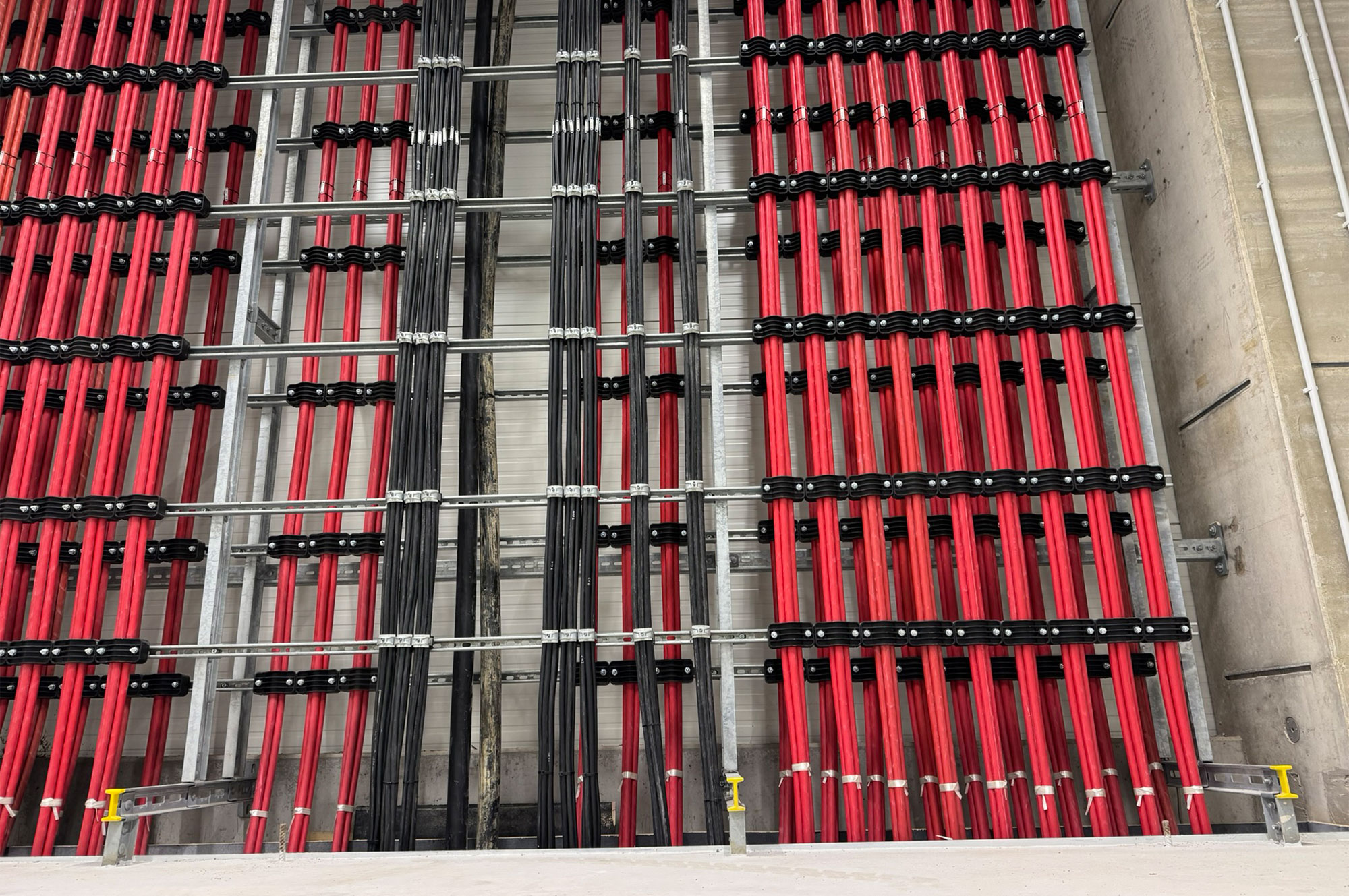 Anordnung von roten und schwarzen Energiekabeln, die in einem strukturierten Regal gelagert sind, mit klaren Trennungen zwischen den Kabeln.