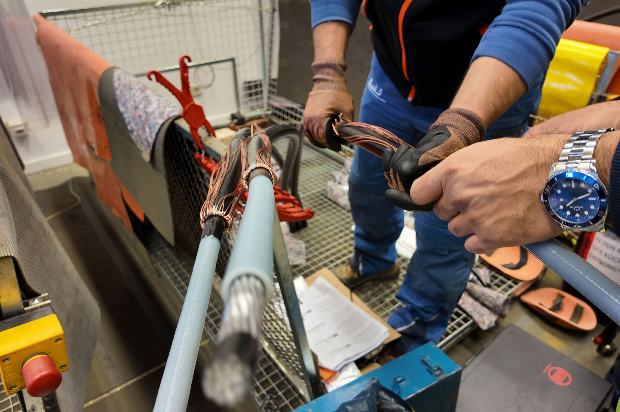 Zwei Hände, die Kabel mit Kupferdrähten verbinden, während sie an einem Arbeitstisch in einer Werkstatt stehen.