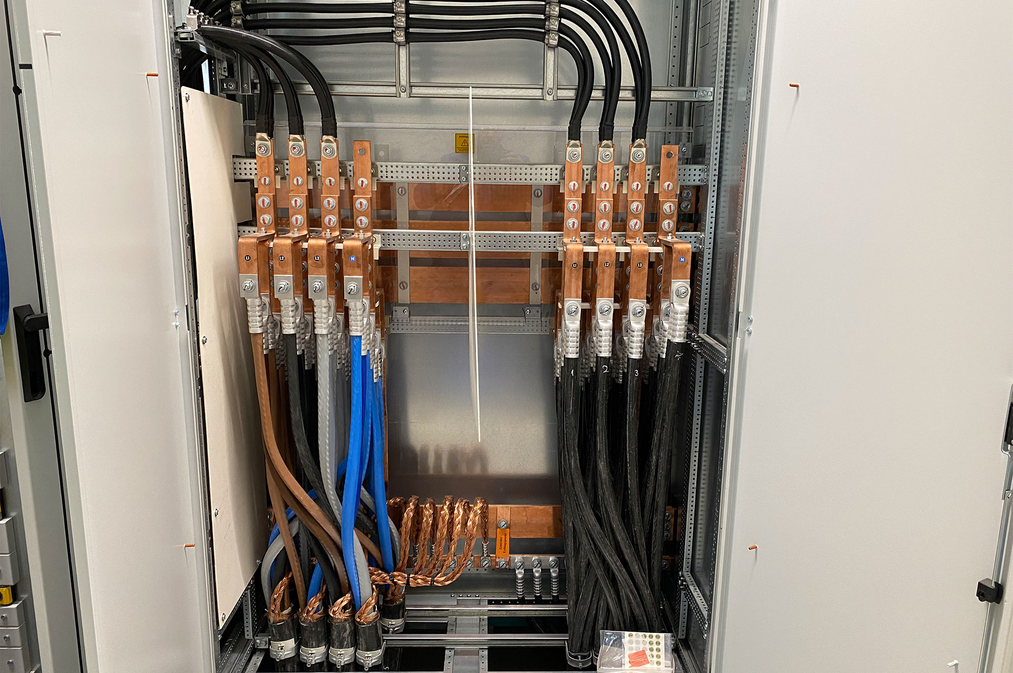 Verteilerkasten mit verschiedenen Kabeln, darunter Kupfer- und Stromkabel in unterschiedlichen Farben, ordentlich angeordnet.