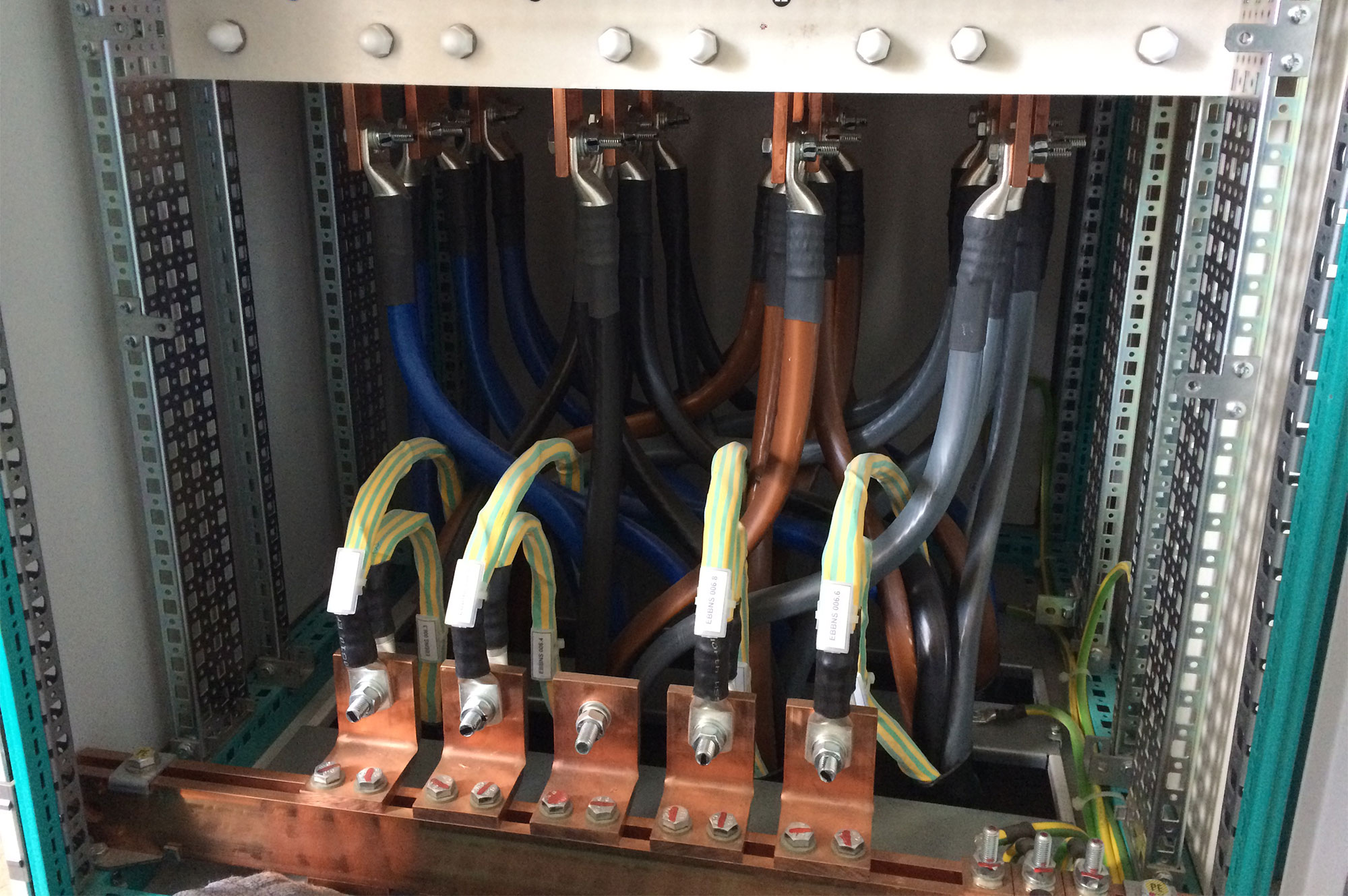 Verkabelung in einem elektrischen Schaltschrank mit verschiedenen Kabeln in Blau, Braun und Grau, die an Kupferanschlüssen befestigt sind.