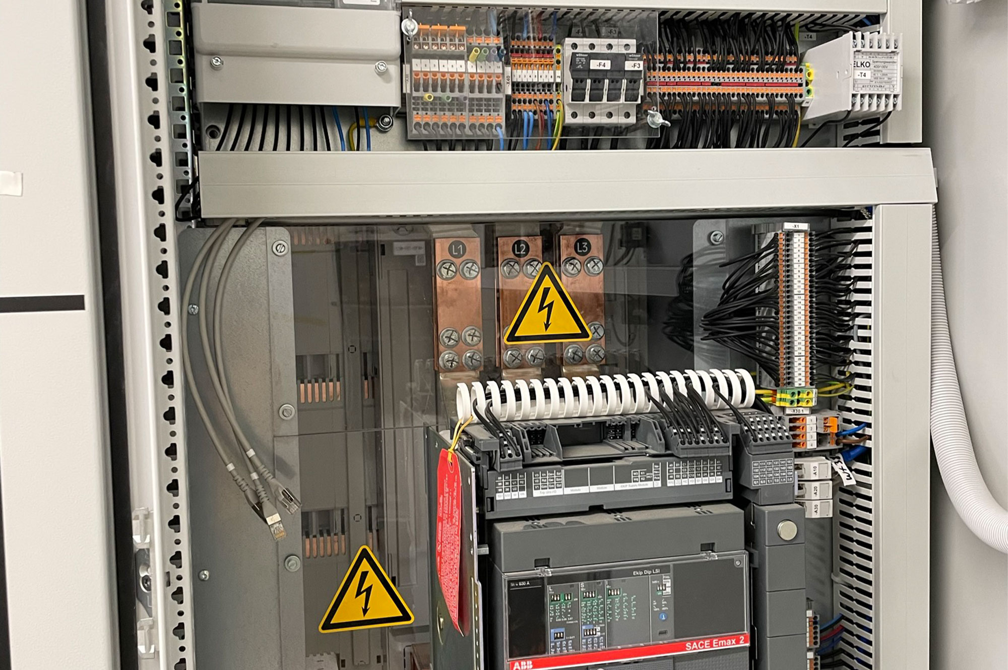 Schaltschrank mit elektrischen Komponenten, einschließlich Sicherungen, Relais und Kabelverbindungen, sichtbar hinter einer transparenten Abdeckung.