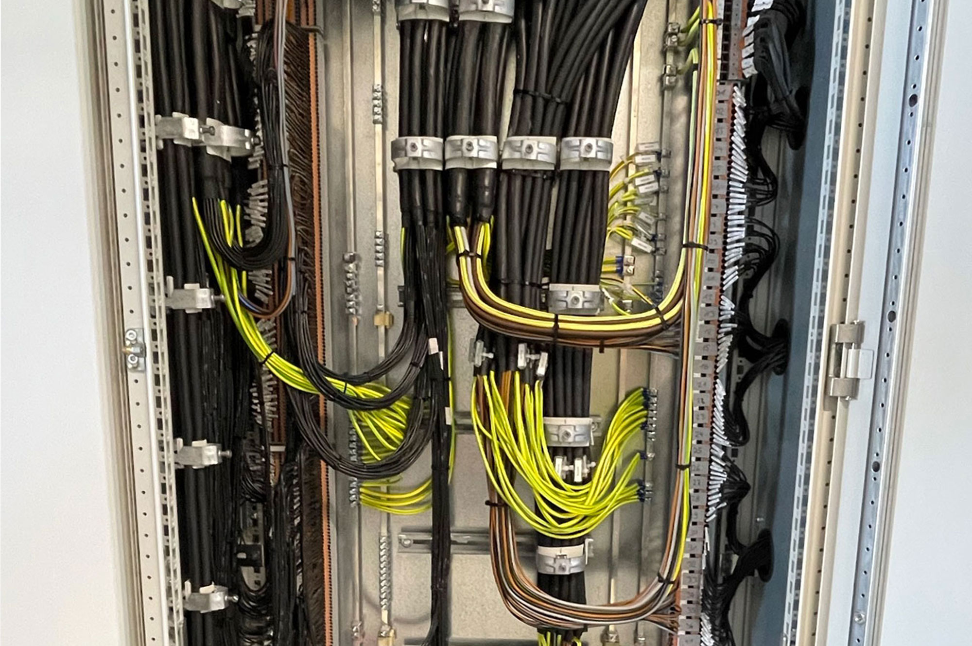 Verkabelung in einem Verteilerkasten mit verschiedenen Kabeln in Schwarz und Gelb, ordentlich angeordnet und gesichert.