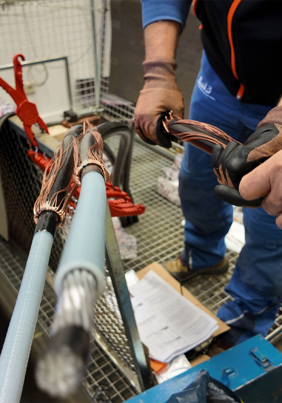 Zwei Hände, die Kabel mit Kupferdrähten verbinden, während sie an einem Arbeitstisch in einer Werkstatt stehen.