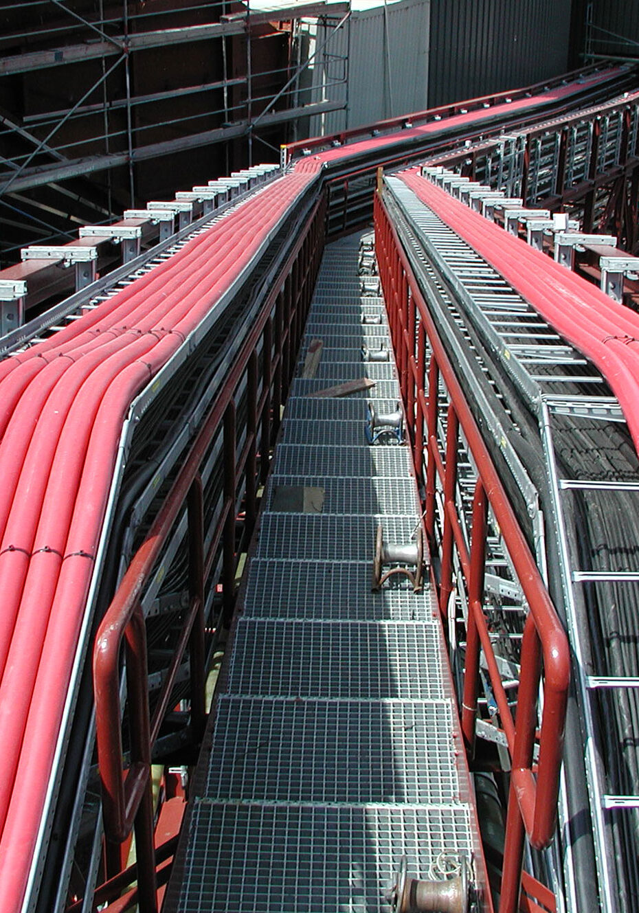 Rote Kabelkanäle auf einer Kabeltrasse in einer industriellen Umgebung, die sich über eine Metallstruktur erstrecken.